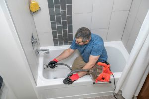 Plumber drain cleaning a bathtub with a plumbers snake